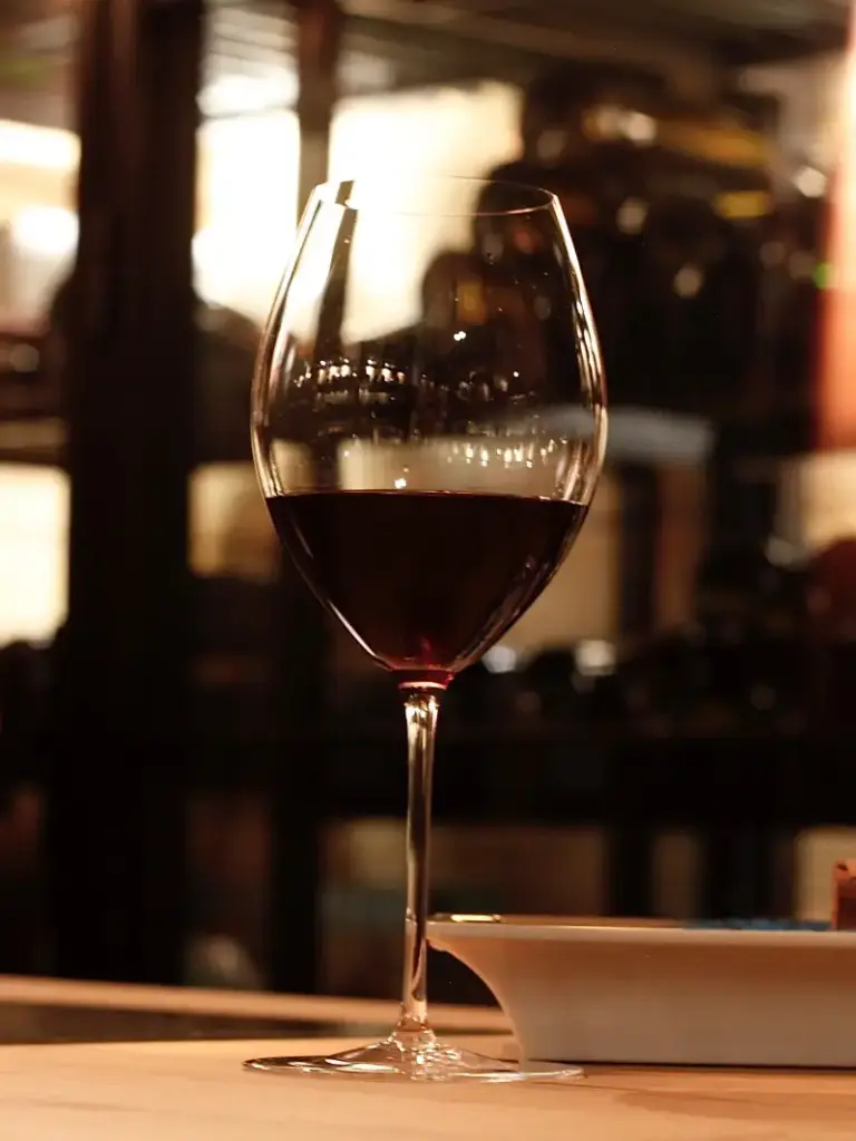 Glas Rotwein auf einem Tisch, im Hintergrund beleuchtete Weinregale